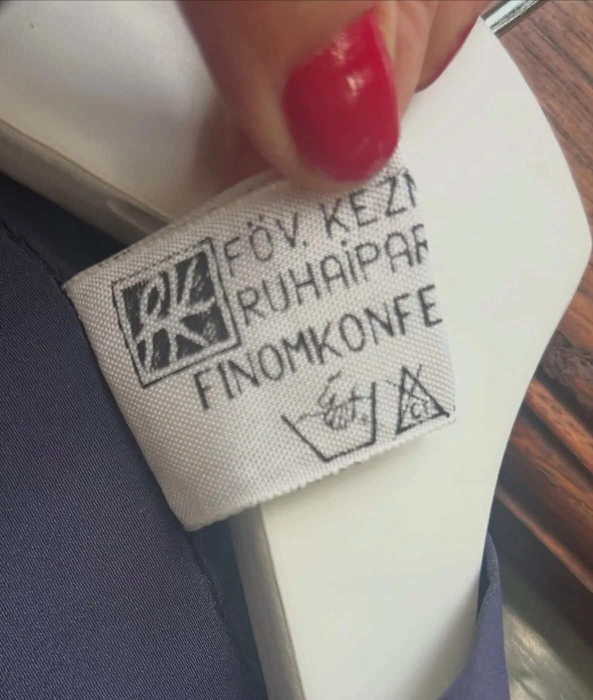 Kéz tartja egy régi magyar ruhacímke fotóját: FŐV. KÉZI RUHAIPARI FINOMKONFEKCIÓ.